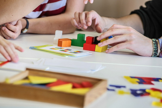 Two people build something with small wooden cubes.