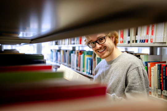 A student stands in front of a bookshelf in the library.