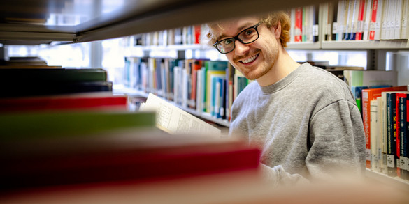 Ein Studierender steht an einem Bücherregal in der Bibliothek.